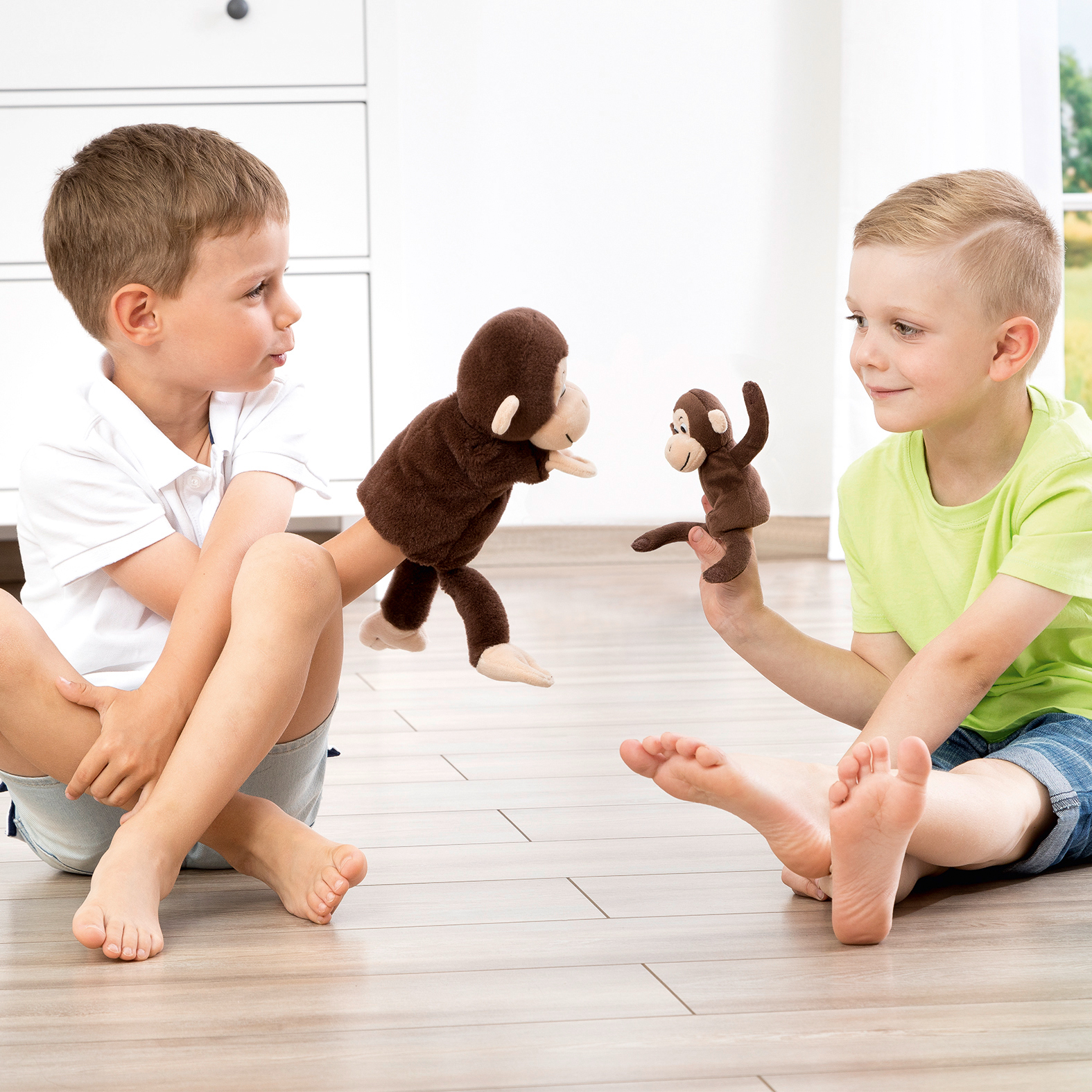 Two children facing each other playing with the Beleduc story hand puppet monkey Cheeta, usage example