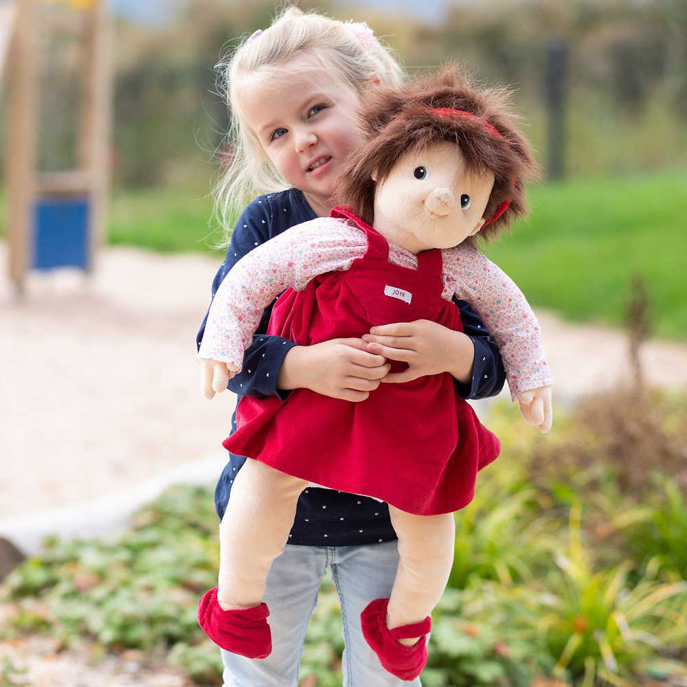 Kind trägt die Joyk Empathiepuppe Ingrid auf dem Arm im Freien