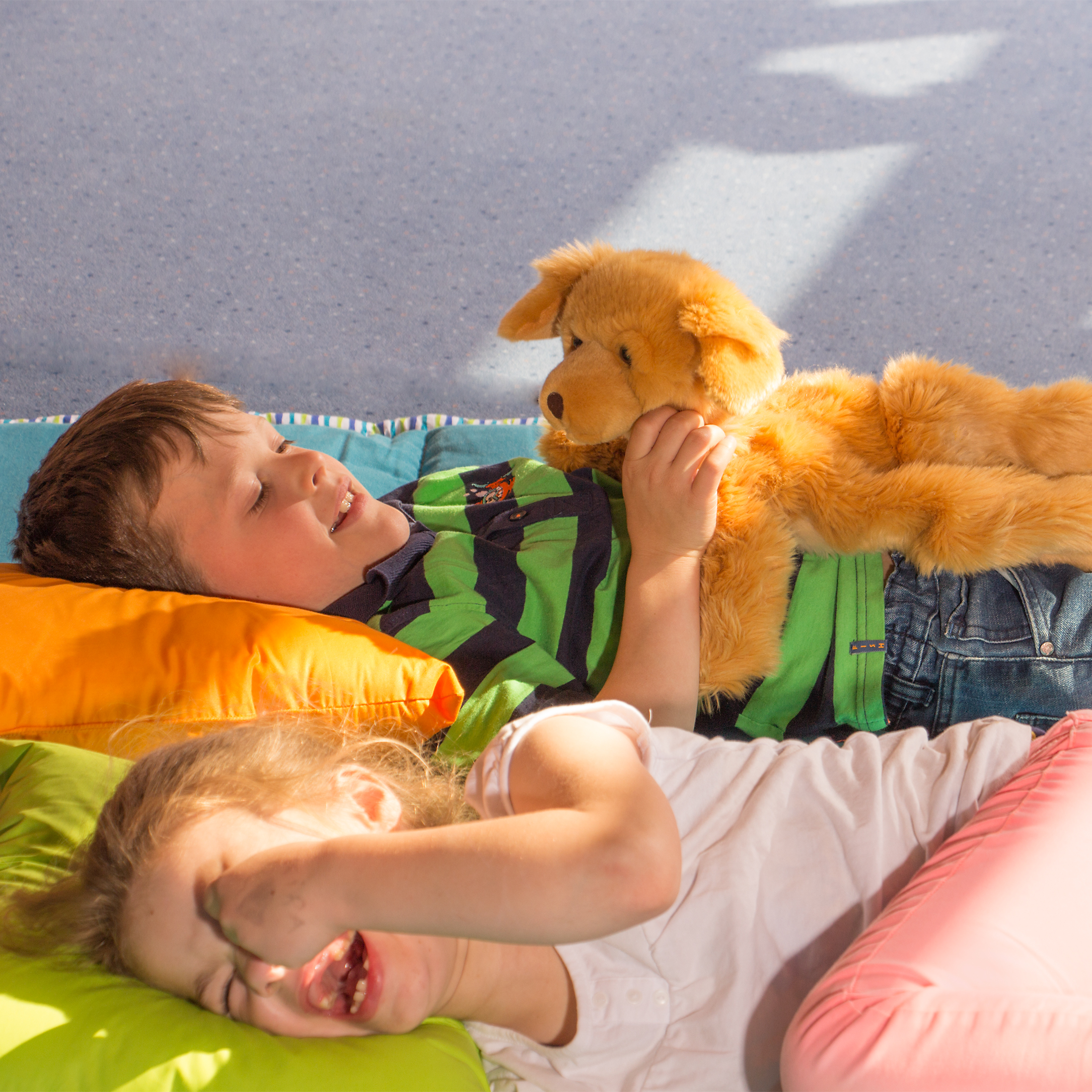Kinder spielen liegend mit der Joyk Empathiepuppe Brando, einem goldbraunen Hund