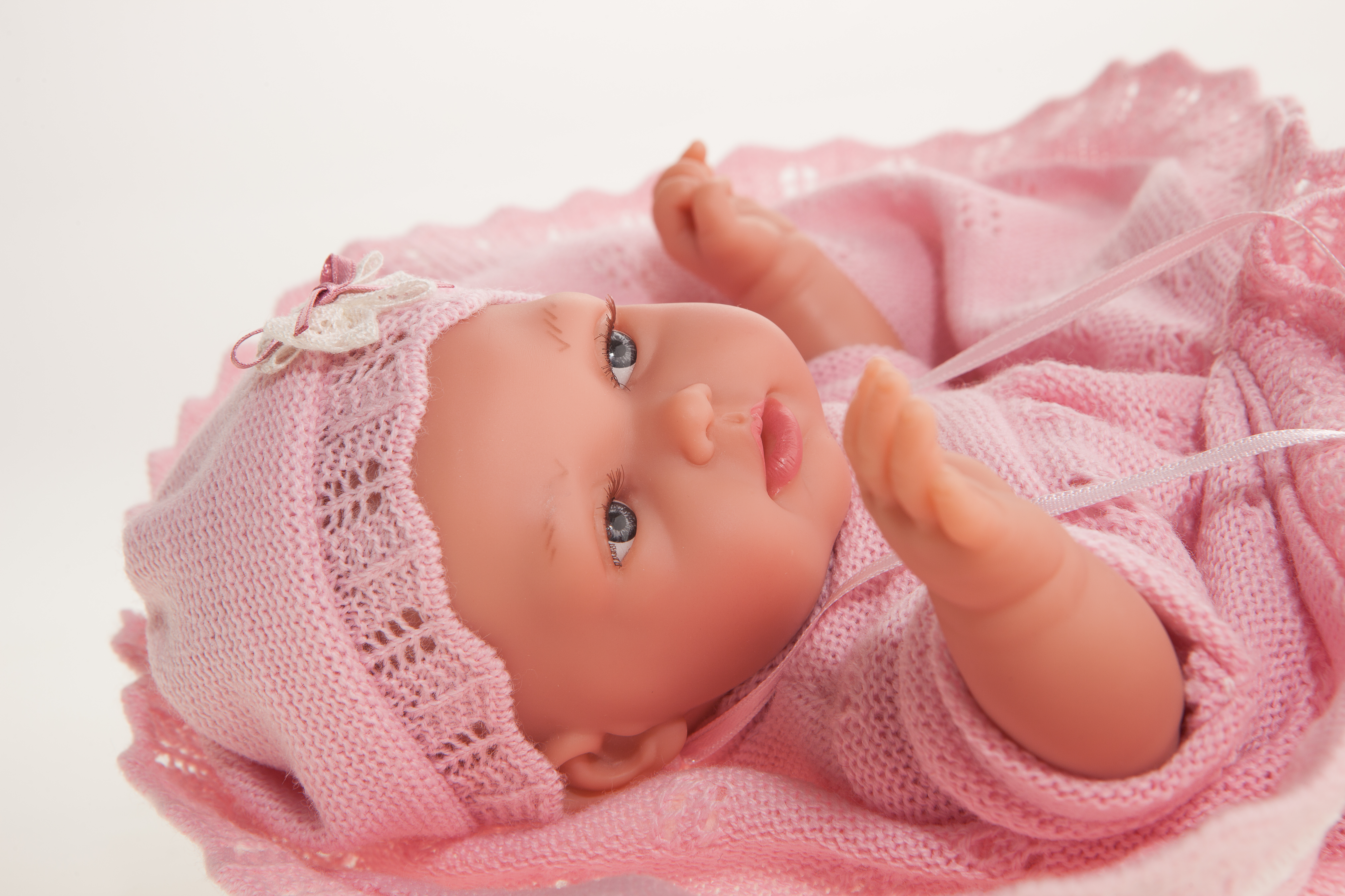 Antonio Juan baby doll Peke, close-up of the doll lying down with pink bonnet, hand close to the mouth