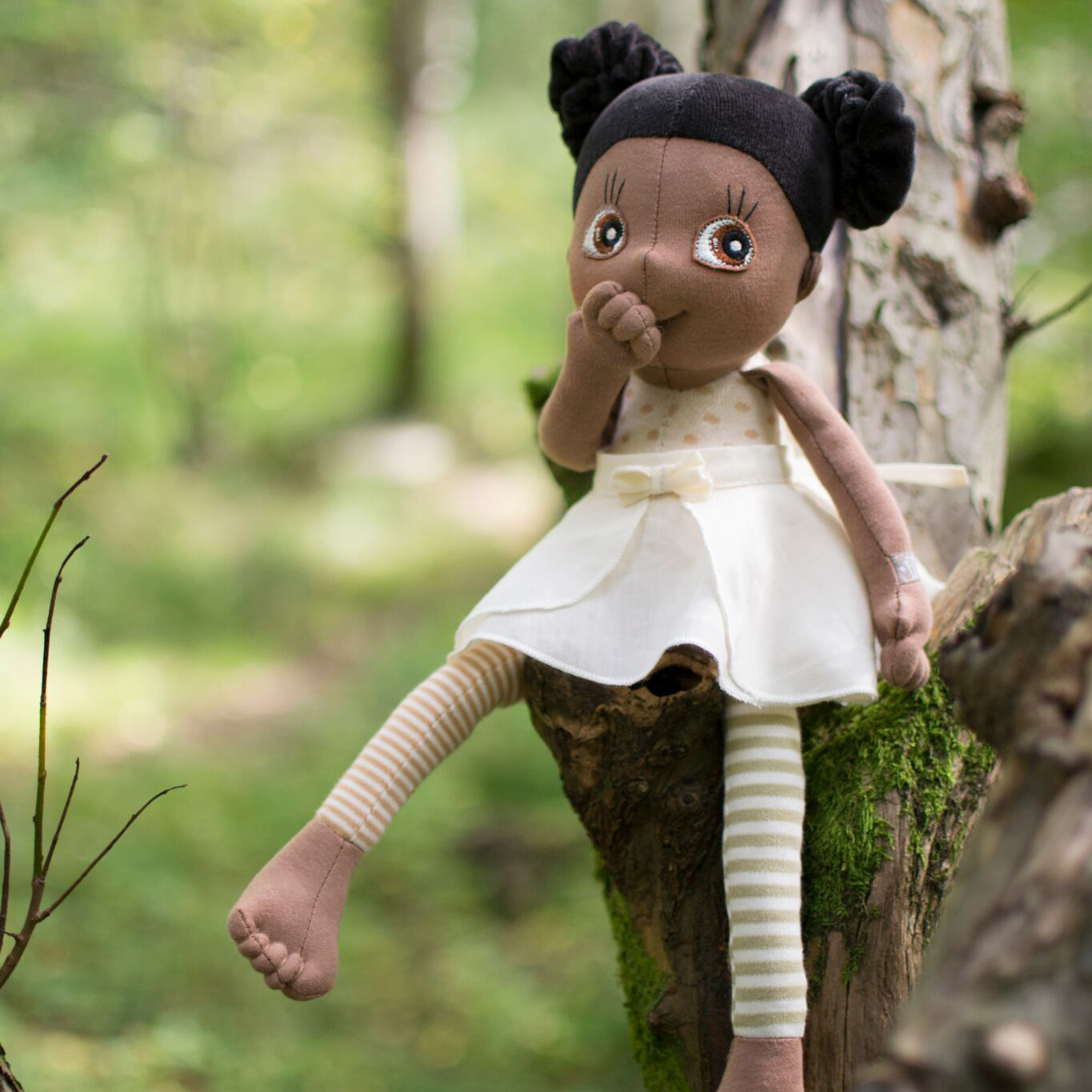 Die Rubens EcoBuds Puppe Poppy sitzt an einem Baumstumpf im Wald