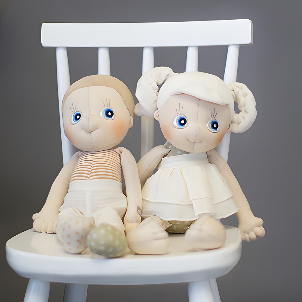 Zwei Rubens EcoBuds Puppen sitzen auf einem weißen Kinderstuhl nebeneinander