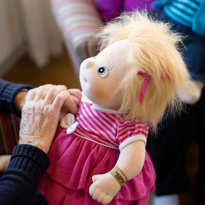 Seniorin berührt die Rubens Barn Original-Puppe Ida im pinken Kleid