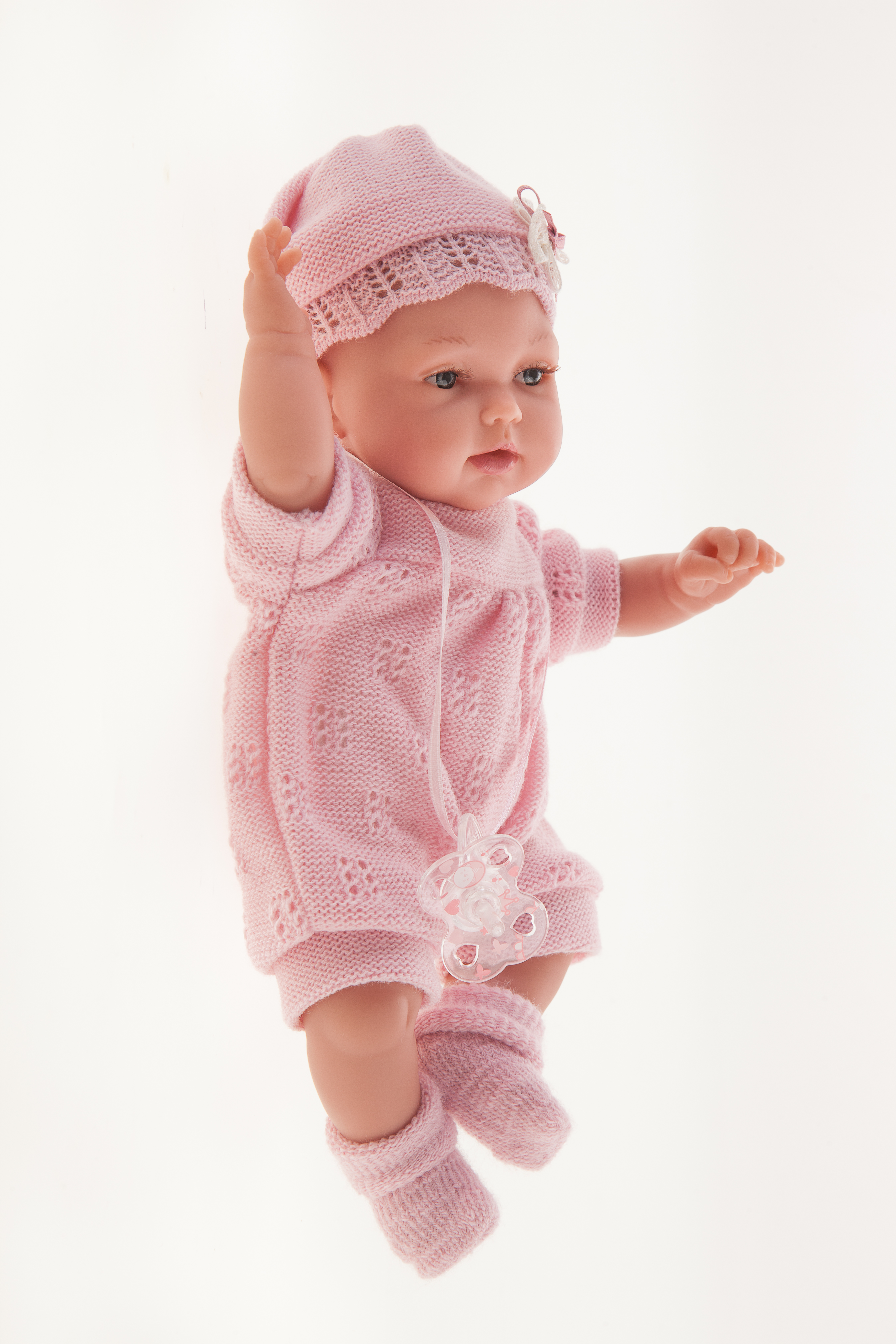 Antonio Juan baby doll Peke, realistic doll in a pink knit outfit, side view with arm raised overhead against a white background