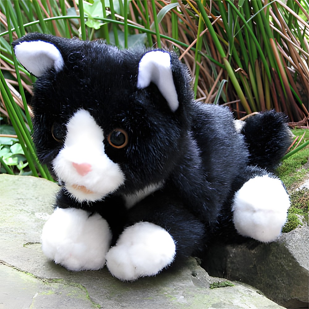 Living Puppets Handpuppe schwarz-weiße Katze auf einem Stein liegend, mit Gräsern im Hintergrund, Außenaufnahme