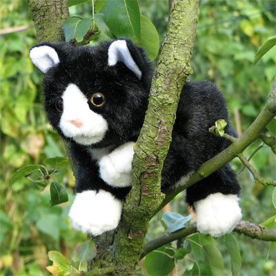 Living Puppets Handpuppe schwarz-weiße Katze auf einem Ast zwischen grünen Blättern sitzend, Außenaufnahme