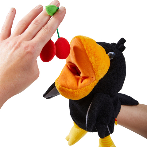 HABA Baby-Handpuppe Rabe Theo, Nahaufnahme einer Hand, die dem Raben Plüsch-Kirschen ans Maul hält