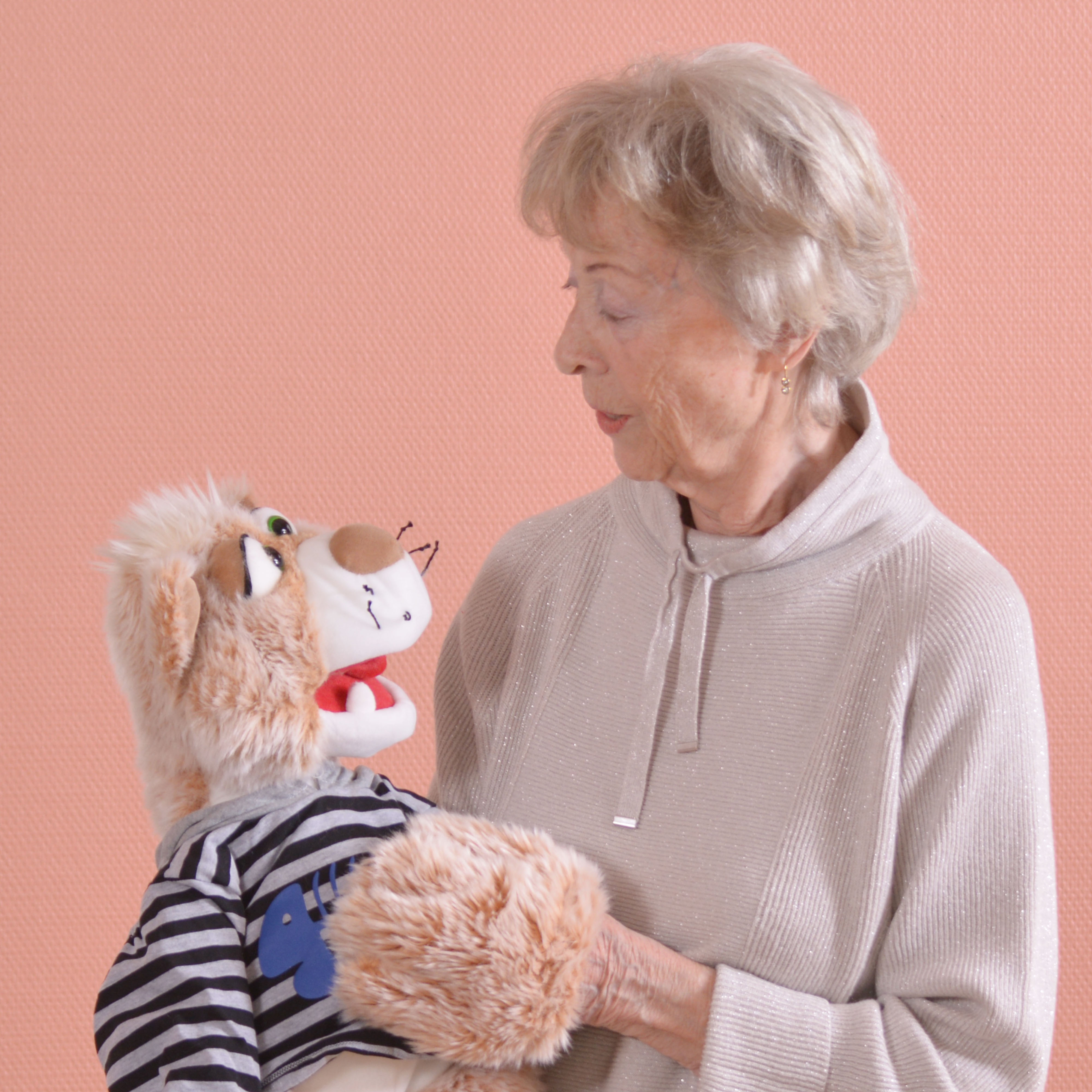 Seniorin hält die Living Puppets Handpuppe Katze Wisky im gestreiften Pullover im Arm, Anwendungsbeispiel