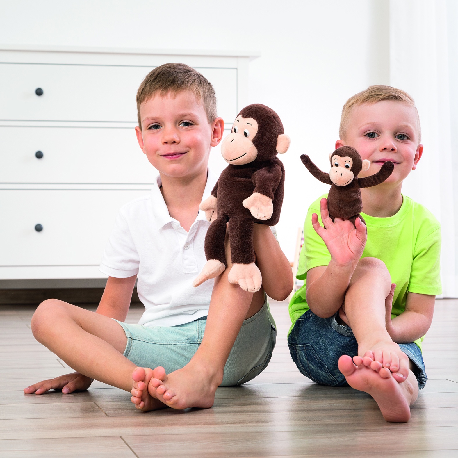 Two boys sitting side by side with the Beleduc story hand puppet monkey Cheeta and finger puppet Bibi, usage example