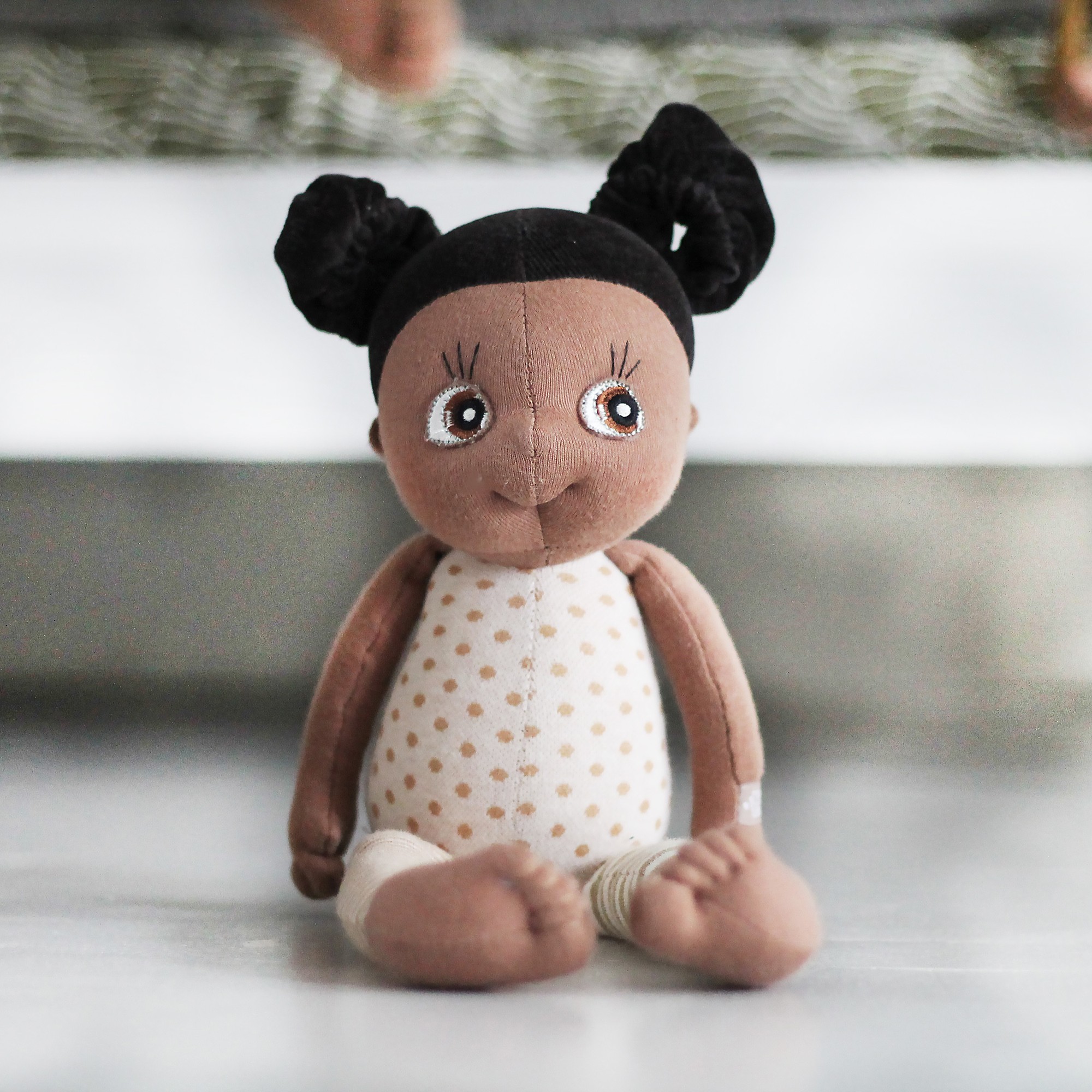 Rubens EcoBuds mini doll Flora sitting with dotted top in front of a bed