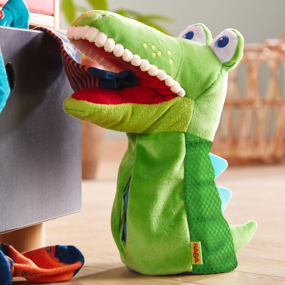 HABA baby hand puppet crocodile Allesfresser, lifestyle photo in a nursery next to a laundry chest