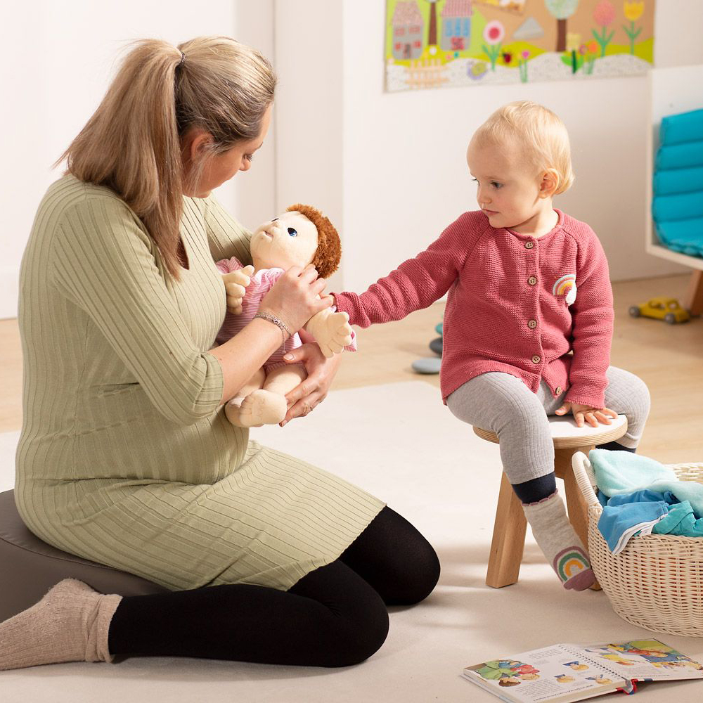 Frau und Kleinkind betrachten die Joyk Empathiepuppe Baby Lilly im Spielzimmer