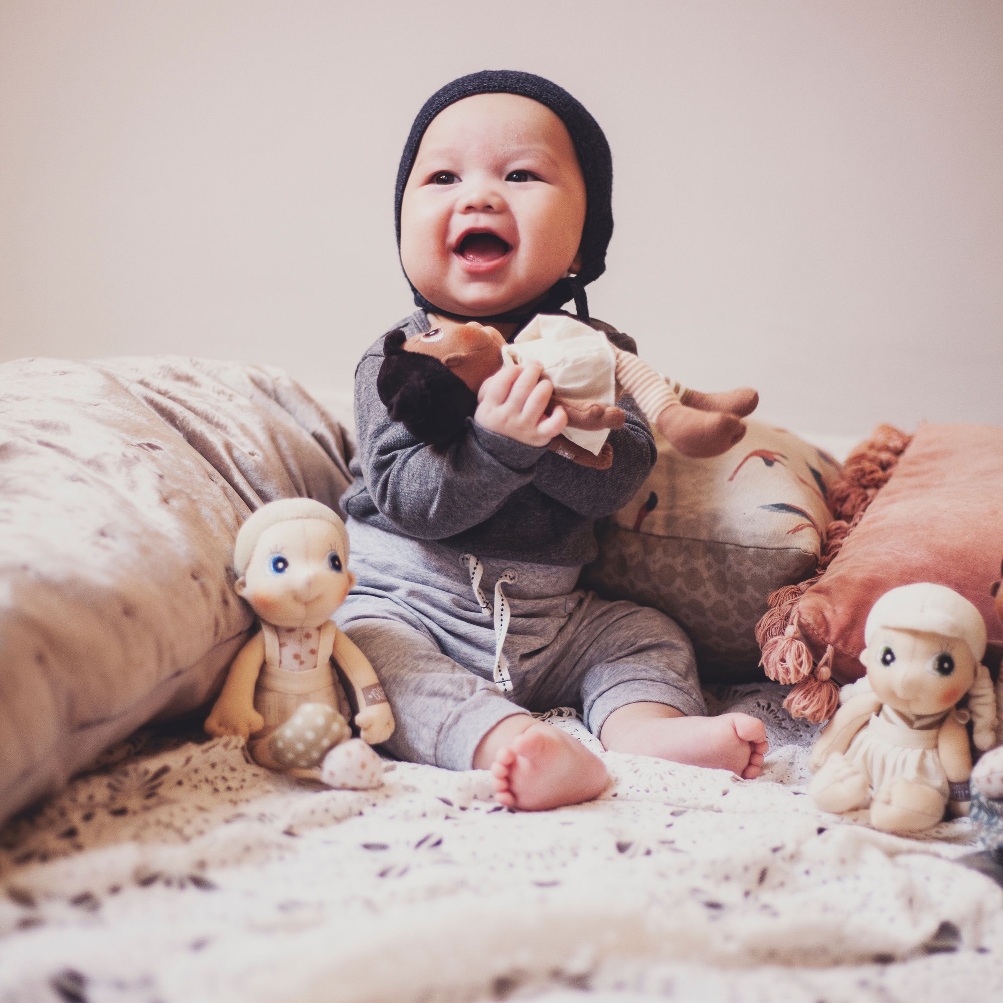Lachendes Baby mit den Rubens EcoBuds Mini-Puppen auf dem Bett