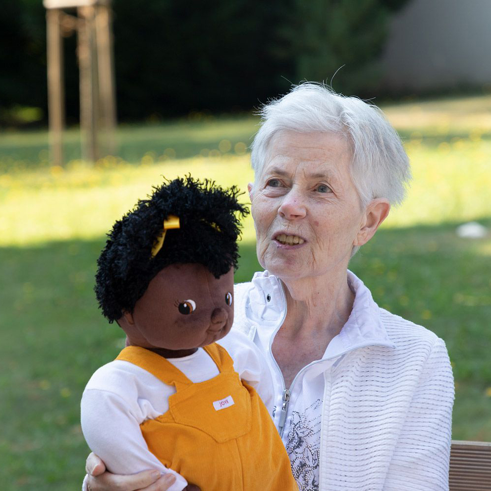Senior lady smiling while holding the Joyk empathy doll Sofia in her arms